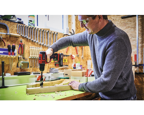 Man boort een gat in een houten plank met een accuboormachine in een werkplaats.