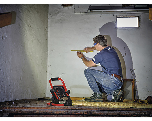 Man meet muur met rolmaat, bouwlamp verlicht de ruimte