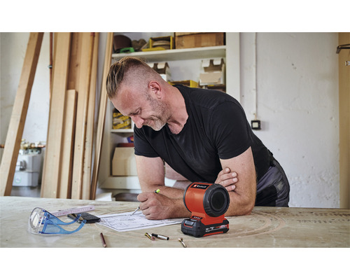 Een man werkt aan een bouwplan met een Einhell acculamp op tafel.