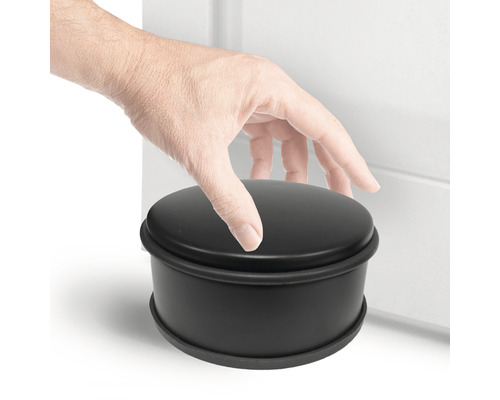 Zwarte ronde deurstopper naast een deur met een hand erop