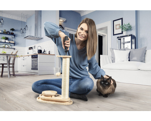 Vrouw monteert een kattenkrabpaal met een schroevendraaier in een woonkamer. Een kat zit ernaast.