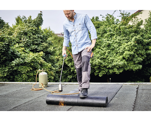 Een man last een dakbaan met een dakbrander op een dak.