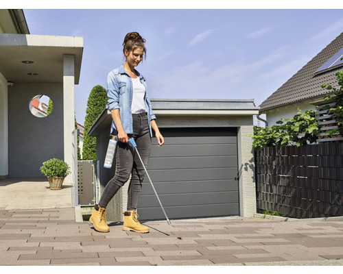 Een vrouw gebruikt een onkruidbestrijdingsmiddel op een trottoir voor een garage.