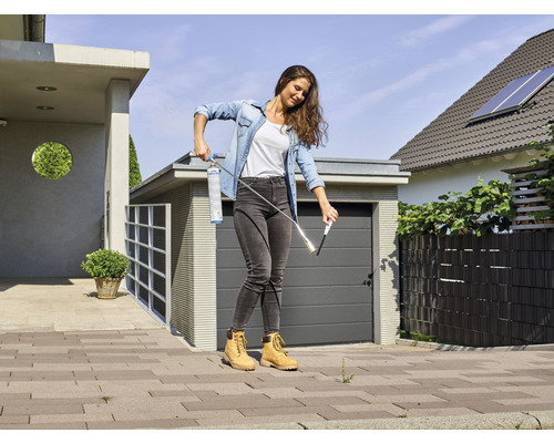 Vrouw verwijdert onkruid met een gasbrander op een bestrate oppervlakte voor een huis.