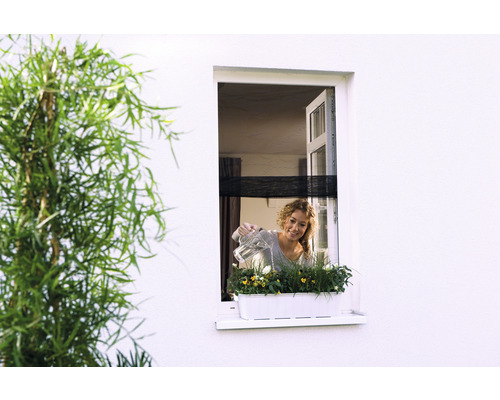 Vrouw geeft bloemen water in een bloembak op een vensterbank.