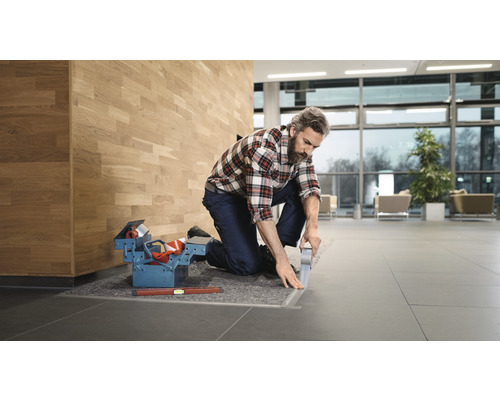 Ambachtsman legt vloerrails in een gebouw, gereedschapskist en waterpas liggen klaar.