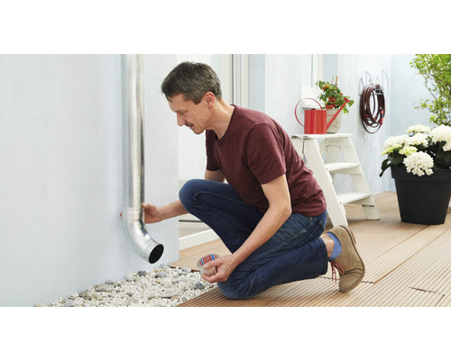 Een man bevestigt een regenpijp aan een buitenmuur van een huis.