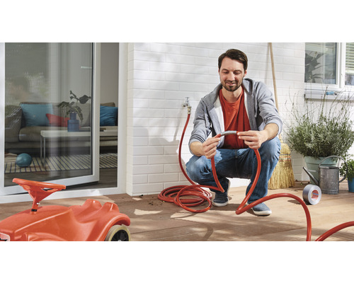 Man repareert tuinslang op terras met speelgoedauto