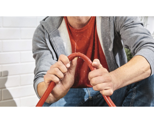 Een persoon houdt een lekkende tuinslang vast.