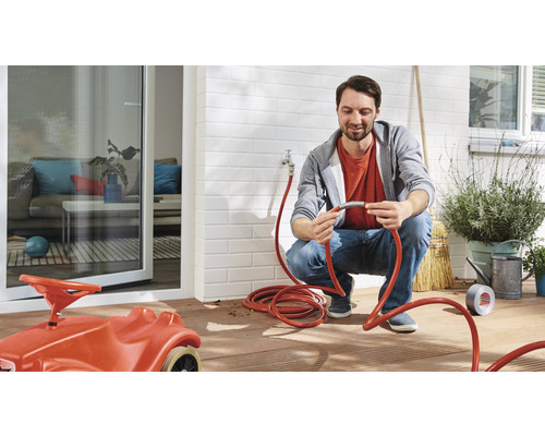 Man verbindt een tuinslang buitenshuis, met kinderspeelgoedauto op de voorgrond