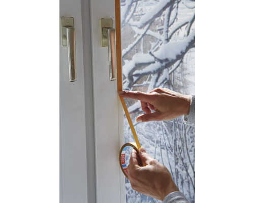 Iemand brengt afdichtband aan op een raamkozijn.