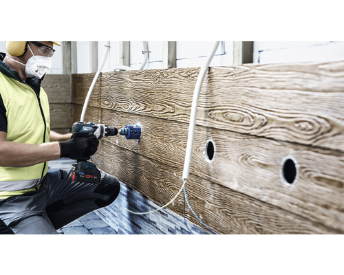 Een man boort met een boormachine een gat in een houten wand voor de installatie van buizen