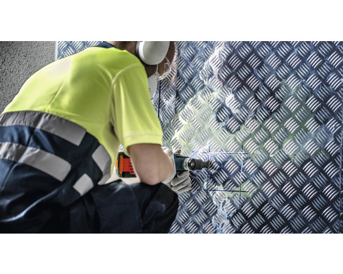 Ambachtsman boort met een multifunctioneel gereedschap in een traanplaatwand