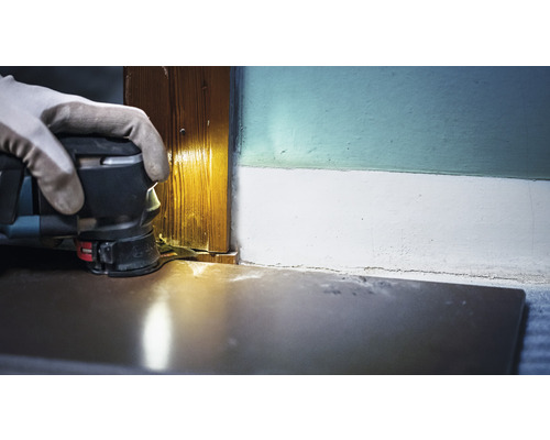 Een persoon gebruikt een multifunctionele schuurmachine om een houten deurpost te schuren.