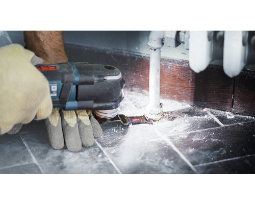 Een persoon gebruikt een multifunctioneel gereedschap op een verwarmingsbuis in de buurt van een muur.