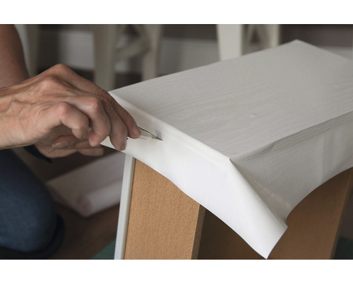 Persoon snijdt folie op een meubelstuk bij met een hobbymes.