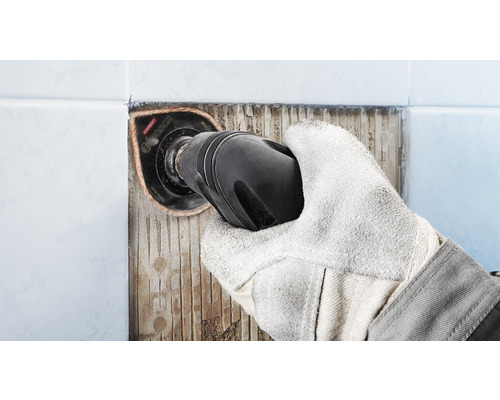 Hand met beschermende handschoen verwijdert tegels met een multitool