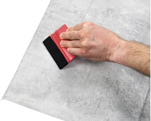 Hand met rakel brengt folie met steenpatroon aan