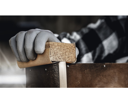 Hand met beschermende handschoen schuurt hout met schuurpapier en kurkblok.