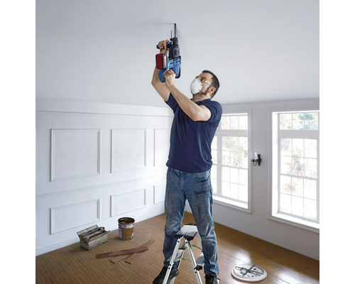 Man boort met een boormachine een gat in het plafond, staand op een ladder.