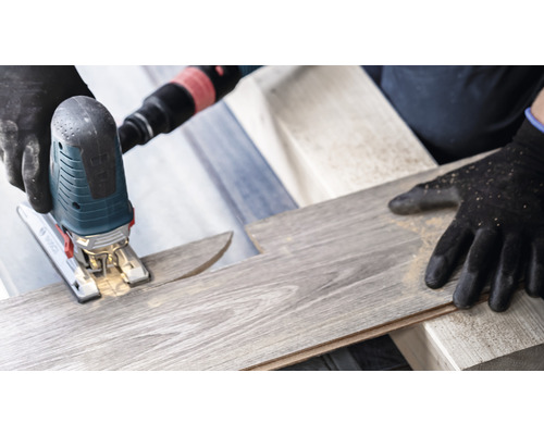 Een decoupeerzaag snijdt een laminaat plank. Er worden veiligheidshandschoenen gedragen.