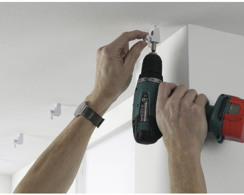 Montage van een gordijnrail met een accuschroevendraaier aan het plafond.