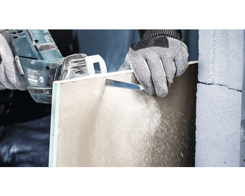 Een persoon zaagt een gipsplaat met een zaag.