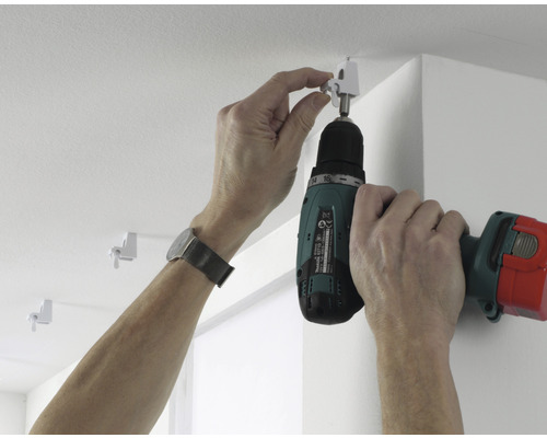 Een persoon bevestigt met een accuschroevendraaier een gordijnroede aan het plafond.