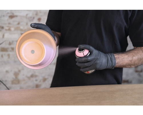 Iemand spuit met een spuitbus verf op een bloempot.