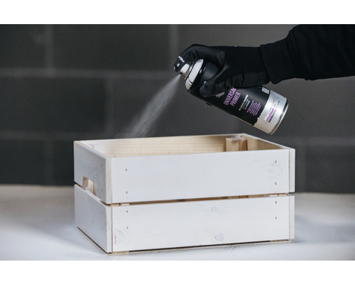 Een persoon spuit een houten krat met universele primer.