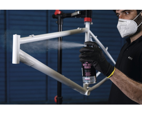 Een persoon spuit een fietsframe met een primer spuitbus.