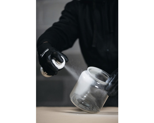 Iemand spuit verf uit een spuitbus in een open glazen pot.