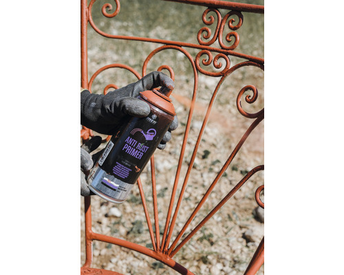 Een persoon spuit een metalen rooster met antiroestprimer