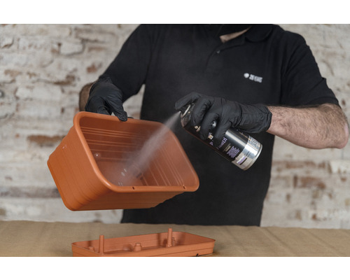 Een persoon spuit een plantenbak met spuitverf.