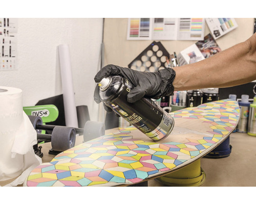 Een persoon draagt handschoenen en spuit acrylvernis op een skateboard.