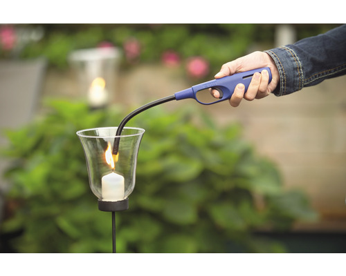 Een persoon steekt met een staafaansteker een kaars in een glas aan.