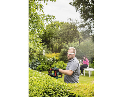 Man snoeit heg met heggenschaar in de tuin.