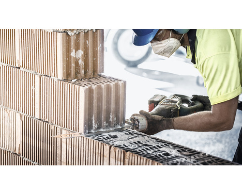 Een bouwvakker zaagt een baksteen met een zaag.