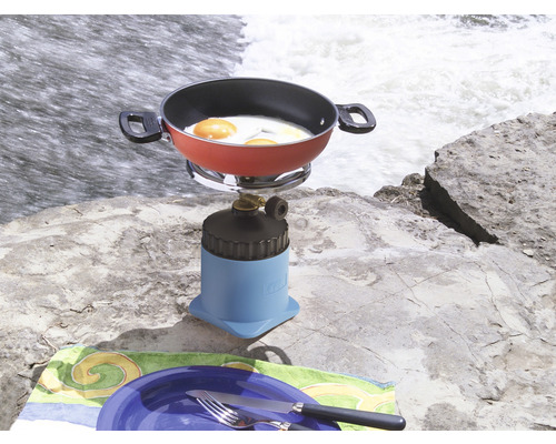 Campingkooktoestel met koekenpan en spiegeleieren op een rots naast een waterval