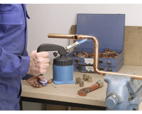 Ambachtsman soldeert koperen buizen met een soldeerbrander, pijpentang en koperen fittingen op een werkbank