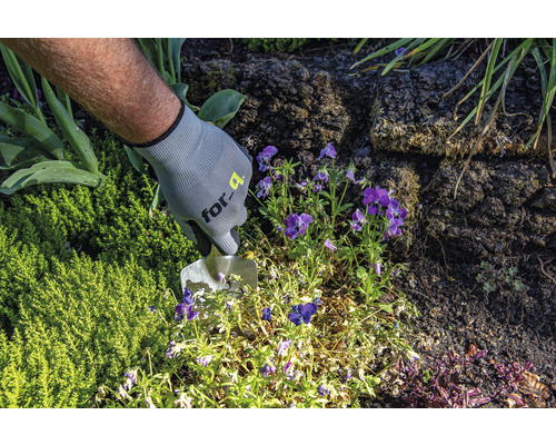 Een persoon met tuinhandschoenen werkt met een planttroffel in de tuin.