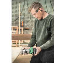 Een man gebruikt een accufrees voor houtbewerking, terwijl hij een veiligheidsbril en oorbeschermers draagt.