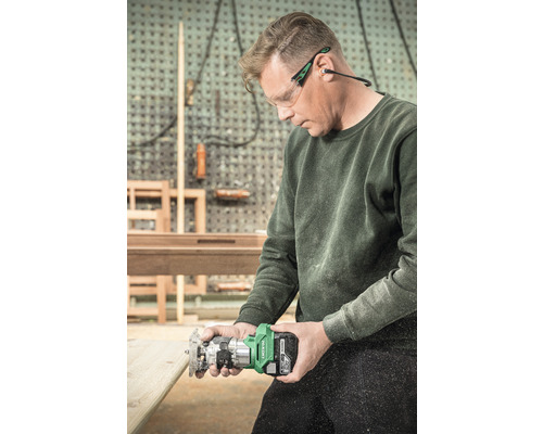 Een man gebruikt een accufrees voor houtbewerking, terwijl hij een veiligheidsbril en oorbeschermers draagt.