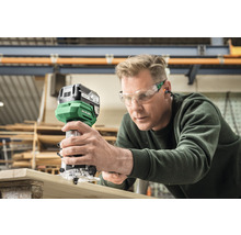 Man gebruikt bovenfrees op houten plank. Hikoki Logo.