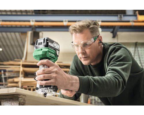 Man gebruikt bovenfrees op houten plank. Hikoki Logo.