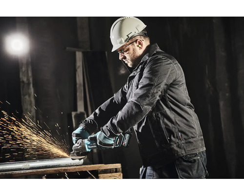Een man met veiligheidshelm, veiligheidsbril en gehoorbescherming slijpt een metalen buis met een haakse slijper.