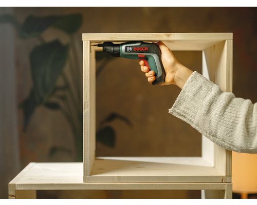 Iemand monteert een houten plank met een accuschroevendraaier van het merk Bosch.