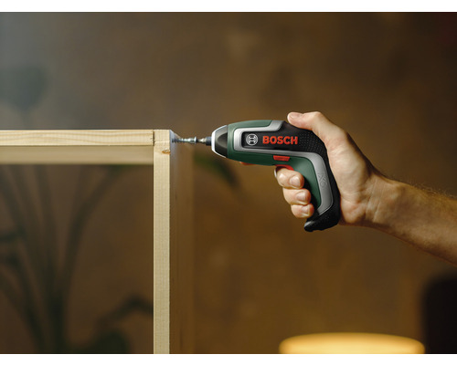 Iemand schroeft met een accuschroevendraaier van Bosch een schroef in een houten plank.