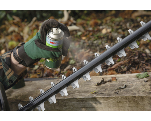 Iemand spuit het mes van een heggenschaar in met een onderhoudsspray van Bosch.