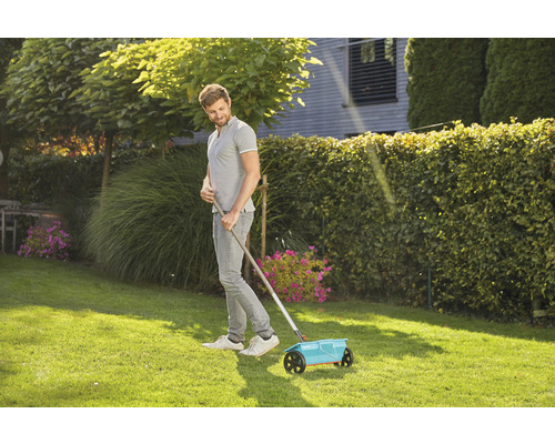 Man gebruikt een meststrooier op een gazon.